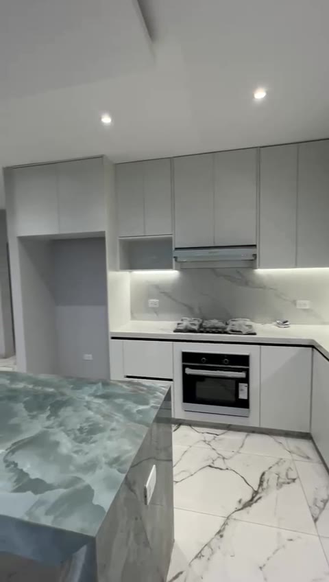 Finished kitchen with green-stone island and under-cabinet lighting — model residence, October 2026